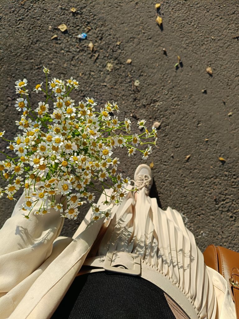 Stylish woman in beige attire holding daisies on a sunny day.